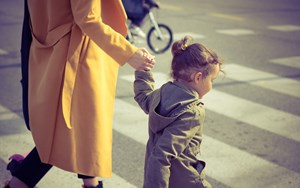 A child holds her mother's hand while crossing the road at a zebra crossing