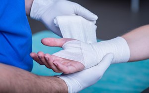 A person has their hand wrapped by a medical professional