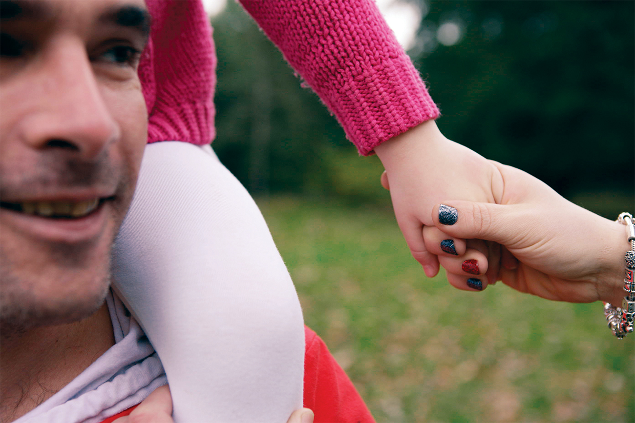 Man with girl on shoulders holding females hand.
